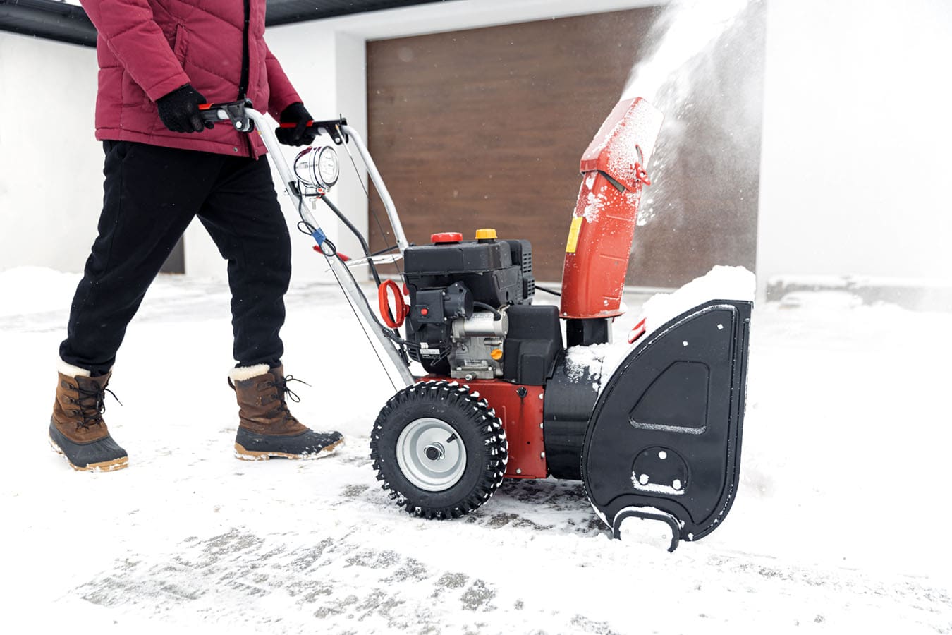 man uses a snowblower to clear snow from his driveway in winter