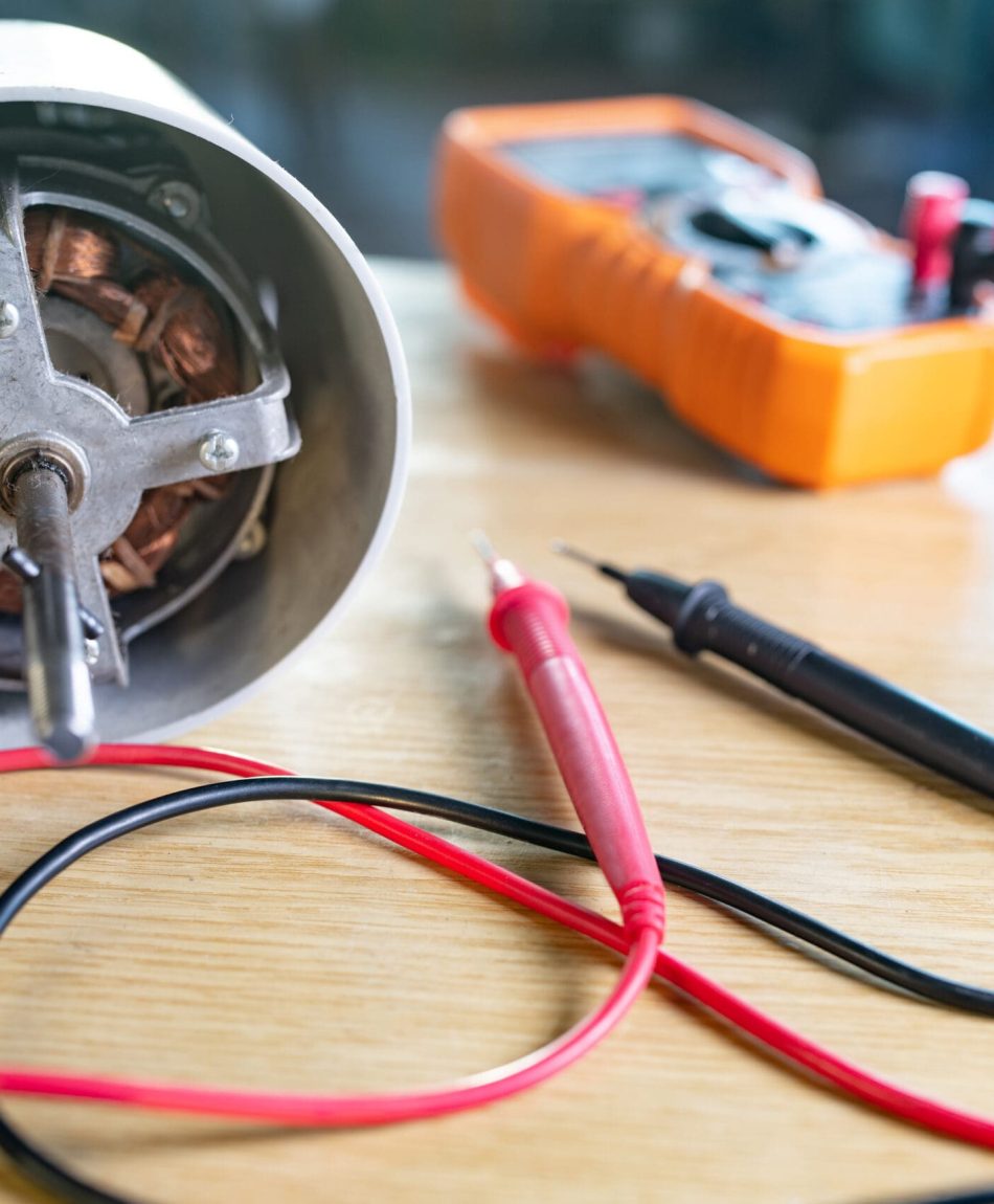 Close-up of iron motor from home cooling fan lies on a table under repair Close-up of an iron motor from home cooling fan and testind tools lies on a table during repair in a specialized workshop. The concept of repair and restoration of damaged equipment